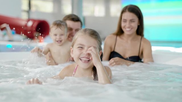 happy family with two little children are swimming in a pool, sitting in small bowl of jacuzzi spraying