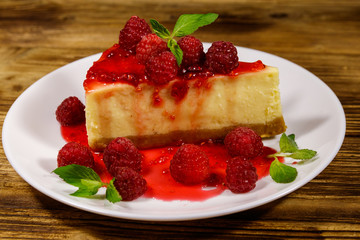 Piece of tasty New York cheesecake with raspberries and raspberry jam in a white plate on wooden table