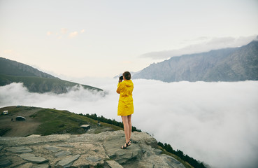 A young Girl in a yellow raincoat photographs the mountains. Georgia. Summer. August. Girl making a photo shoot of mountain. 