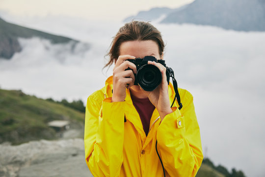 A young Girl in a yellow raincoat photographs the mountains. Georgia. Summer. August. Girl making a photo shoot of mountain. 