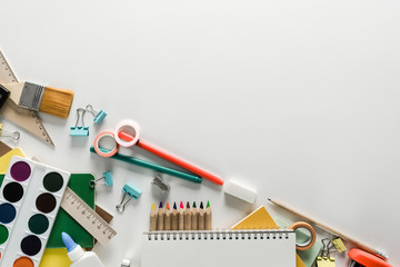 Top view over a school supplies as calculator, rulers, tapes, paper clips, notebooks and other stuff placed at one corner of a white background. Back to school concept. Office supplies flat lay