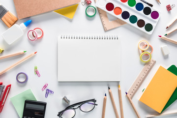 Top view over a school supplies as calculator, rulers, tapes, paper clips, notebooks and other stuff placed in a circle on a white background with notebook in the middle of it. Back to school concept.
