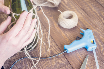 Woman decorating a bottle from wine with an ecological twine. Rustic style, handmade craft. Gift for christmas and other celebrations. Crafting process. Selective focus
