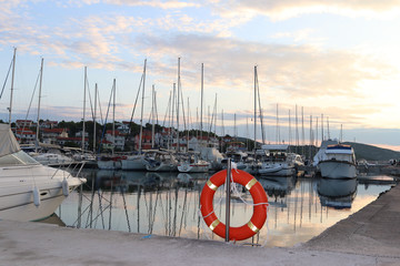 Orange life ring on the pier in the Croatian marina against the backdrop of sailing yachts. Safety...