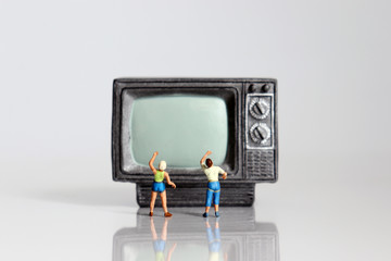 Miniature man and miniature woman pointing hands on miniature television.