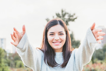 Young attractive woman in light colored sweater welcoming and trying to hug the viewer