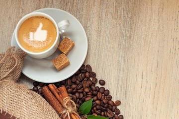 Cup with espresso with coffee beans, burlap sack and cinnamon on light wooden background