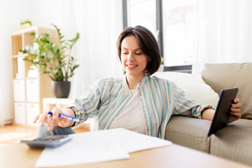 business, savings, finances and people concept - woman with tablet pc, papers and calculator at home