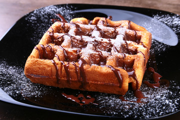 Black plate with homemade belgian waffles with Sifting sugar powder.