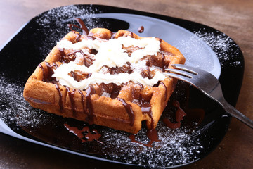 Closeup of homemade Belgian waffles with whipped cream, chocolate sauce and raspberries on black plate. Sweet dessert.