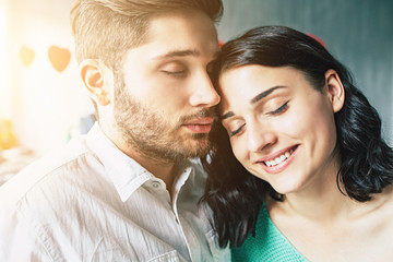 Beautiful young tender lovely couple are kissing and hugging each other while sitting on the floor of bedroom with romantic background. St Valentine's day. Anniversary. Date. Love concept