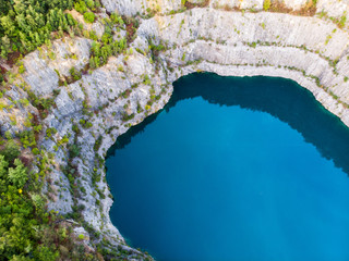 (Laufaufnahme, Drohne) Felswand eines Steinbruchs mit blauem See im Vordergrund © JDM
