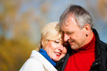 Close-up portrait of beautiful mature wife hugging husband during a bright sunny day