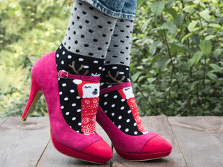 Women's legs in stylish shoes, bright, variegated, multi-colored socks on the wooden terrace on the background of green trees. Lifestyle, fashion, beauty, fun