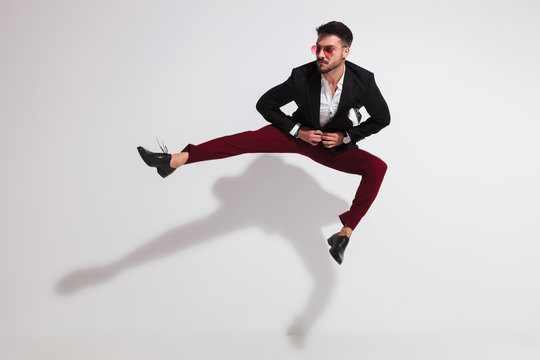 jumping young man parting his legs and unbuttoning black suit