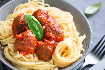 Beef meatballs in tomato sauce with Italian spaghetti and fresh basil leaf on a dinner table. Simply homemade recipe, close up.