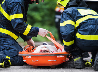 Firefighters putting an injured woman into a plastic stretcher after a car accident.