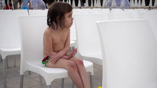Portrait of a child who is cold. Girl 4-5 years after swimming in the pool. A child is sitting on a white chair. Many chairs are places for spectators or sports fans.