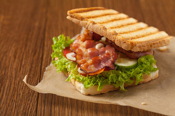 Toasted sandwich with bacon, tomato, cucumber and lettuce.
