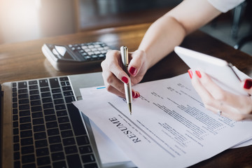 woman holding pen over resume application with smart phone and using computer laptop to job search...