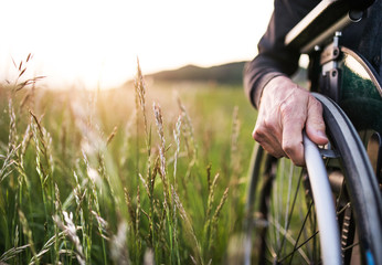 A close-up of man's hand on a wheelchair in nature at sunset. Copy space.
