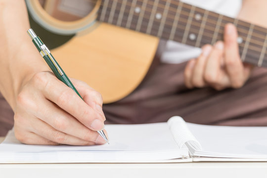 male songwriter hands writing a song on paper while playing acoustic guitar. song writing concept
