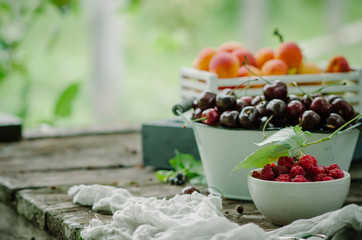 Mix of fresh berries and fruit in vintage wooden box on rustic wooden background. Raw healthy food. Assorted summer berries and fruit.
