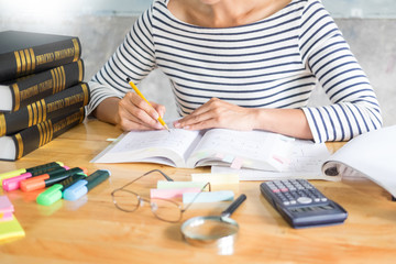 Charming girl sitting by wooden table reading and writting on notebook in a classroom in fornt of a board with formulas.