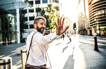 Hipster businessman walking up the street in London, looking back and greeting somebody.