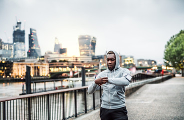 Black man runner with smartphone in an armband on the bridge in London, resting.