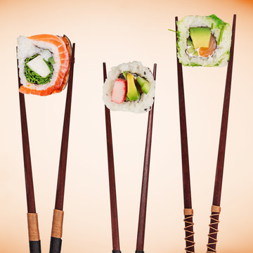 Traditional japanese sushi pieces placed between chopsticks, separated on pastel background.