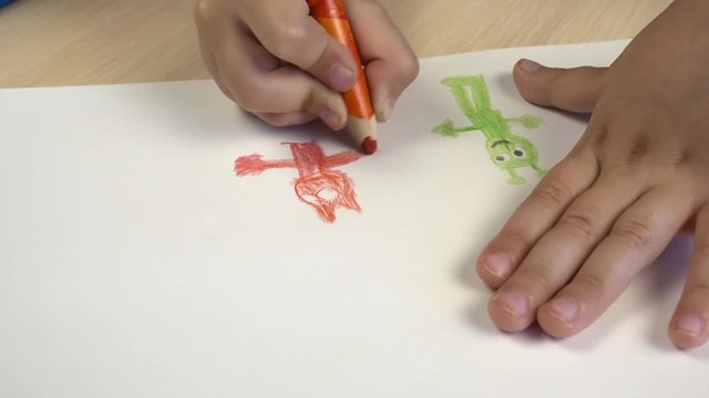 A picture of a child on paper. The view from above, the child draws in colored pencils.