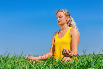 Young woman meditating in grass with blue sky