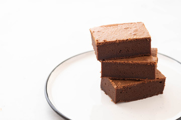Chocolate brownie square pieces in stack on white plate. American traditional delicious dessert. Copy space.