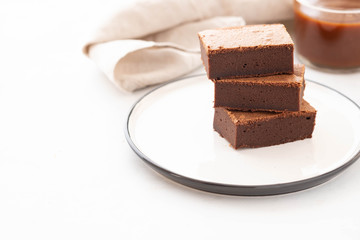 Chocolate brownie square pieces in stack on white plate. American traditional delicious dessert. Copy space.