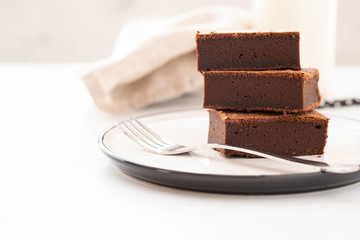 Chocolate brownie square pieces in stack on white plate. American traditional delicious dessert. Copy space.