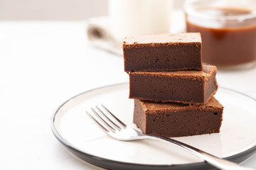 Chocolate brownie square pieces in stack on white plate. American traditional delicious dessert. Copy space.