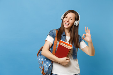 Young cheerful woman student in denim clothes with backpack headphones listen music hold school...