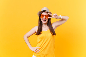 Obraz na płótnie Canvas Portrait of smiling excited young woman in straw summer hat, orange glasses showing victory sign, copy space isolated on yellow background. People sincere emotions, lifestyle concept. Advertising area