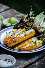 Tasty grilled corn cobs on old table with herb butter and lime on wooden table in the open air.