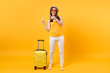 Traveler tourist woman in summer casual clothes, hat with suitcase isolated on yellow orange background. Female passenger traveling abroad to travel on weekends getaway. Air flight journey concept.