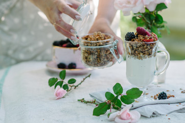 Woman's hands as she eats healthy breakfast .Yogurt with strawberries and granola in a bowl on the table.