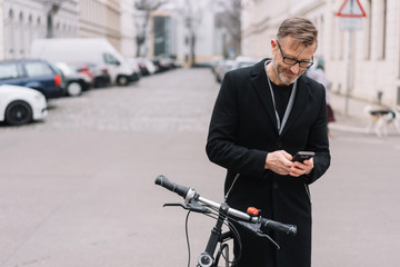 Mature man with bicycle using mobile phone