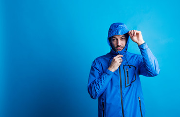 Portrait of a young man in a studio with anorak on a blue background. © Halfpoint