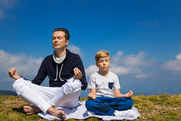 Zen like father and son meditating in lotus position on mountain peak.