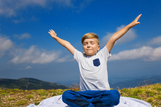 Small boy practicing Yoga in nature. Carefree kid with arms outstretched against the sky.