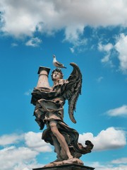 Fototapeta premium Roman sculpture on a blue sky background, located on the bridge over the Tiber river in Rome. On the head of the statue sit gulls, cormorants