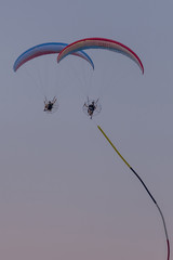 Pair of motorized paragliders against a colorful sunset sky with a banner