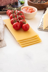Ingredients for Italian lasagna with fresh cherry tomatoes and green basil leaves on sheets of dried pasta. Copy space.
