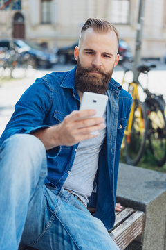 Young bearded man sitting with mobile phone
